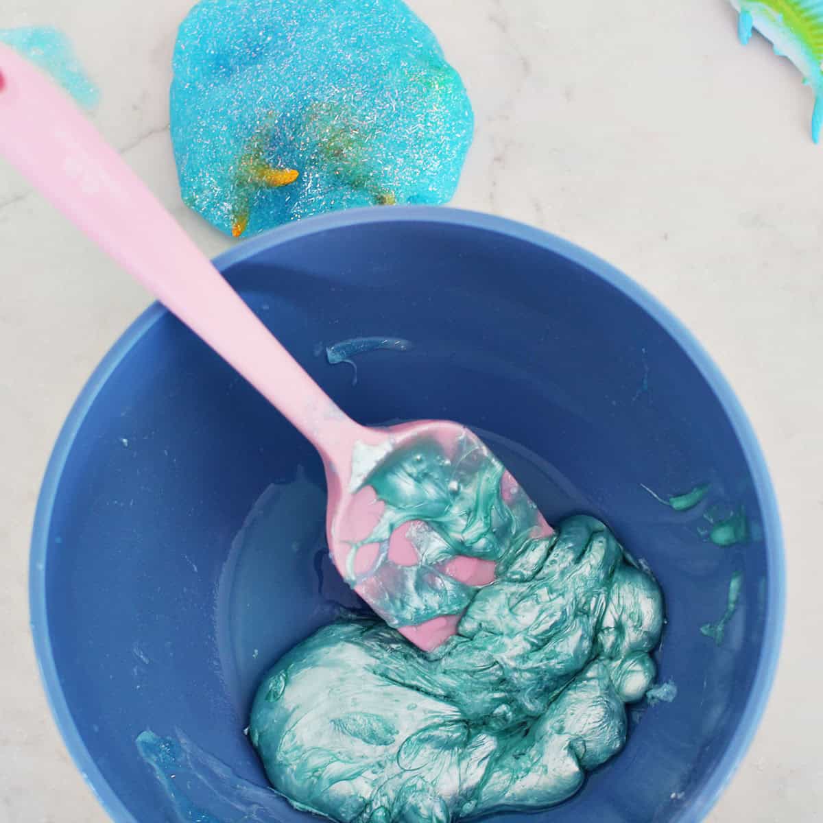 metallic glue in a blue bowl being stirred by a pink spatula.