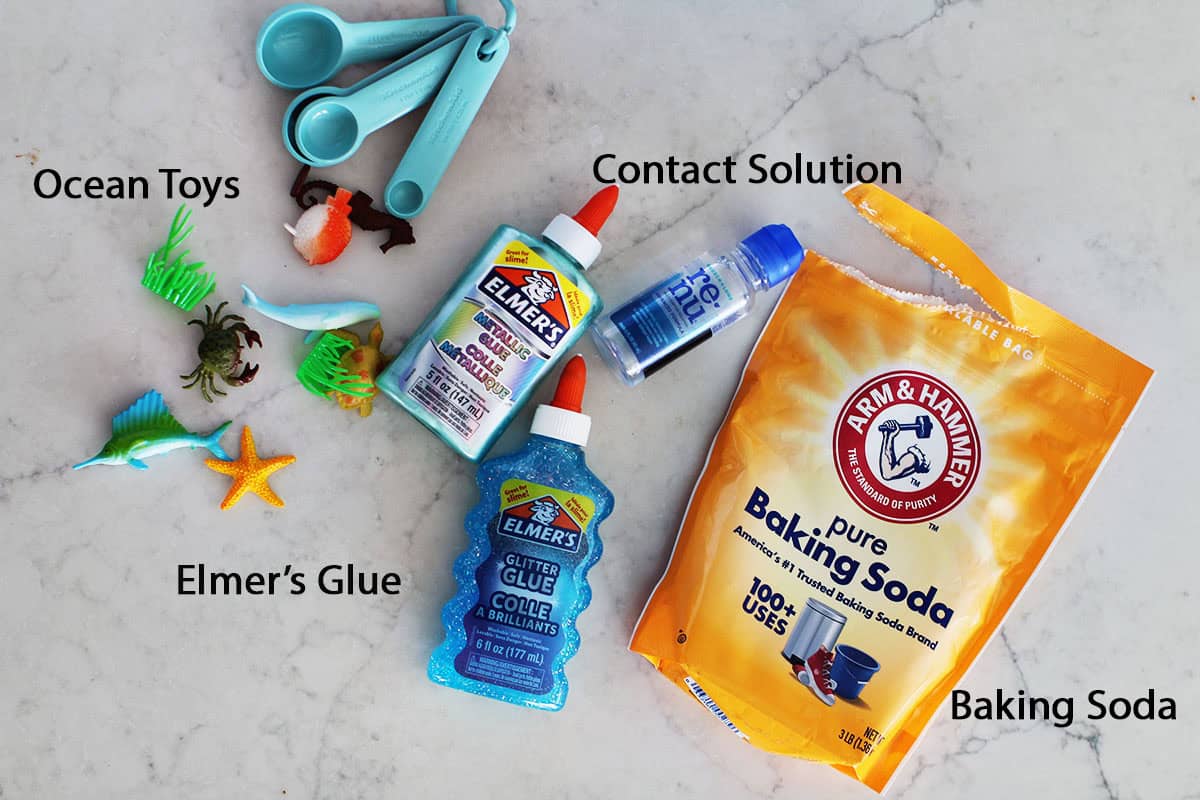 Baking soda, contact solution, glitter glue, mettalic glue and fish toys on a counter.