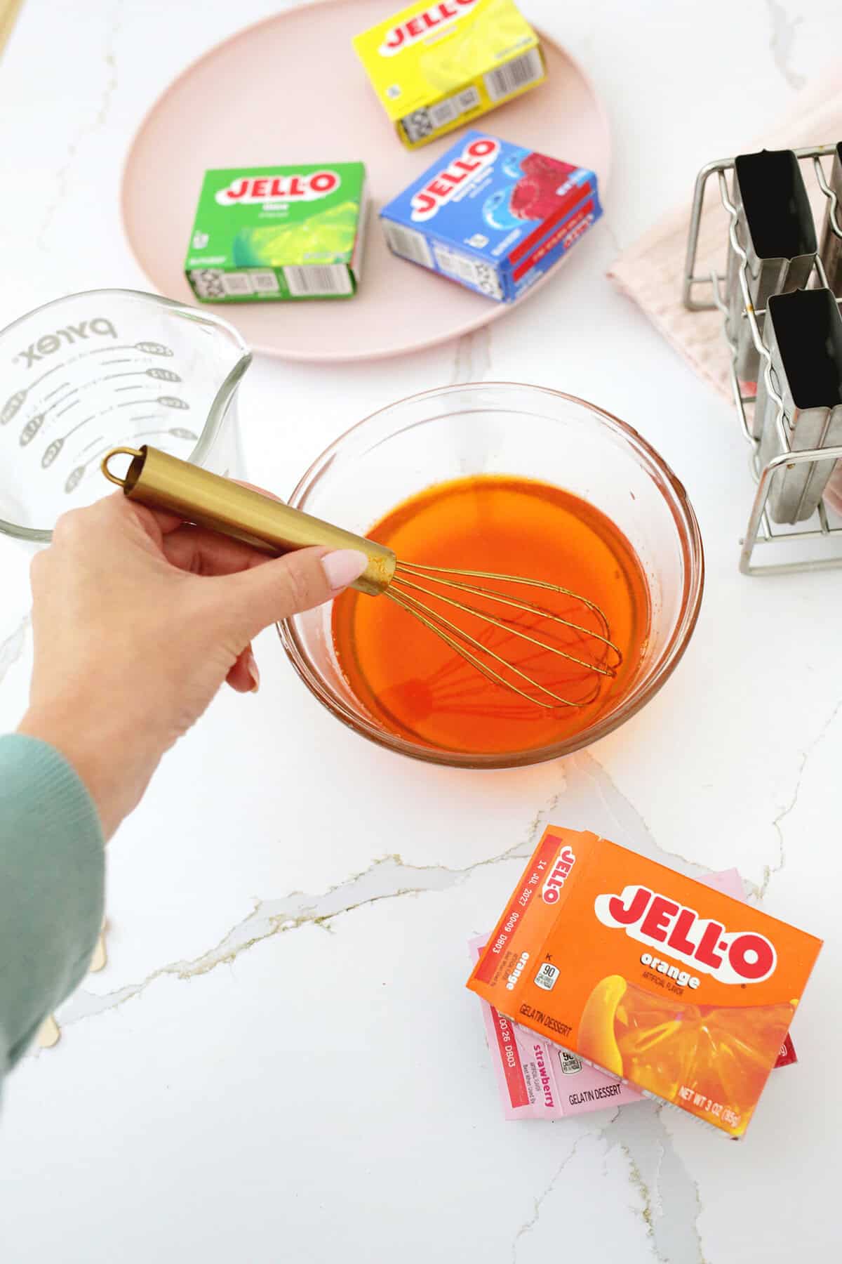 Liquid orange jello being whisked together with a gold whisk.