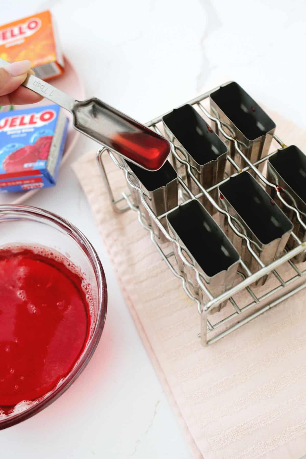 Red liquid jello being added to a silver popsicle mold.