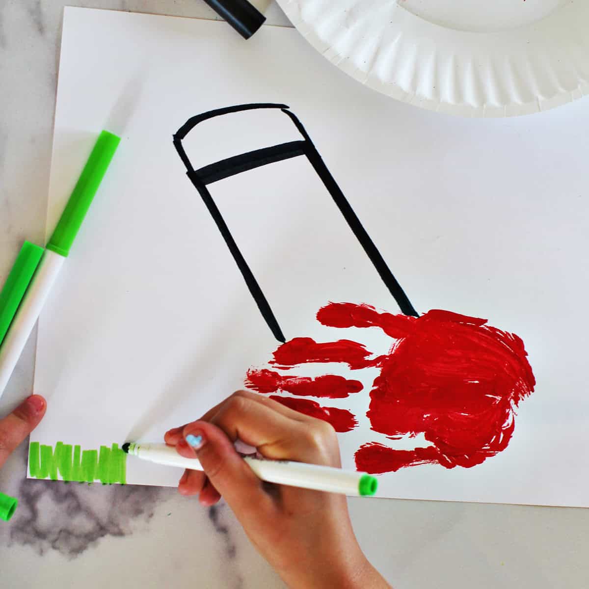 Child drawing green onto a paper to look like grass.