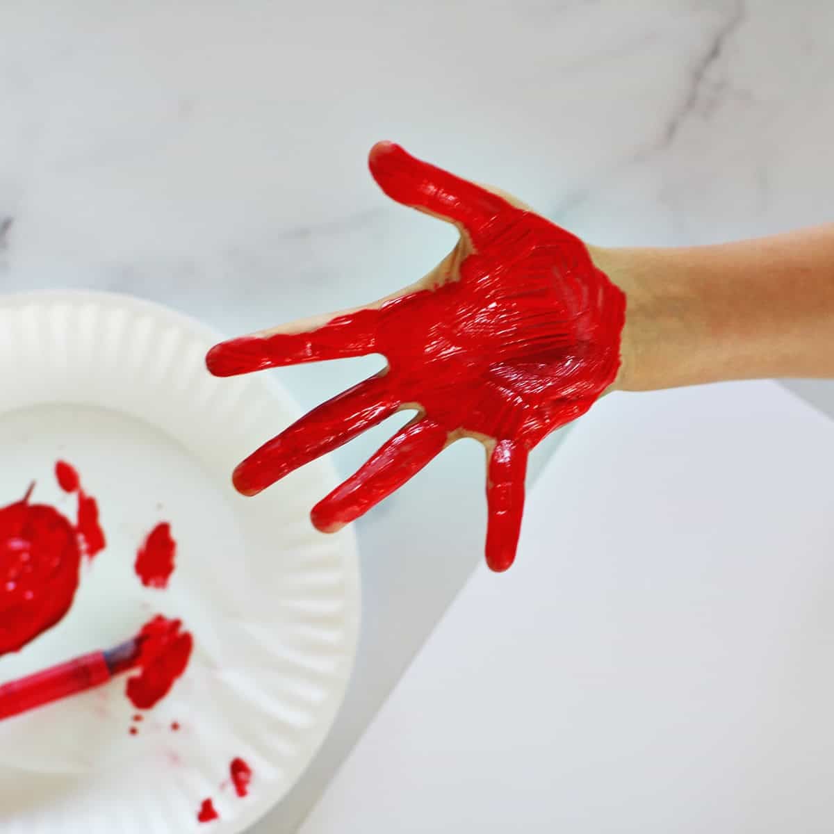 Child's hand painted red held over a paper plate with red paint on it.