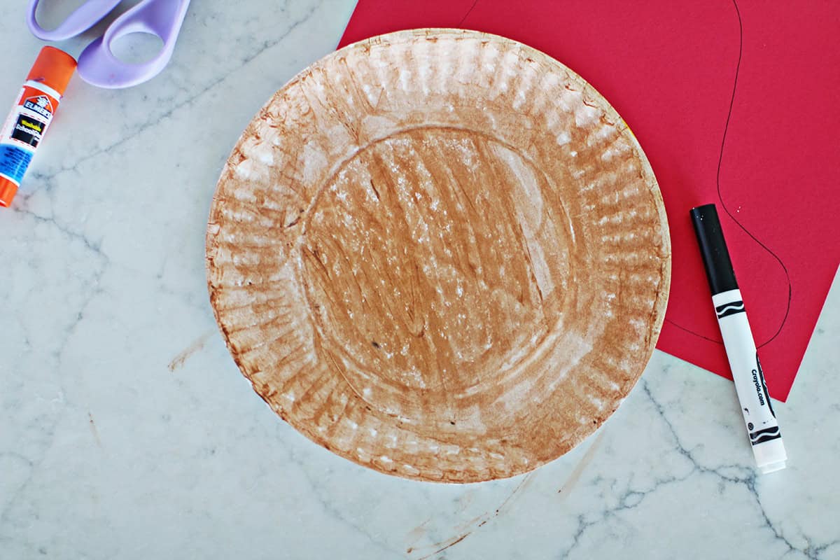 paper plate that has been painted brown next to a marker and a piece of cardstock.