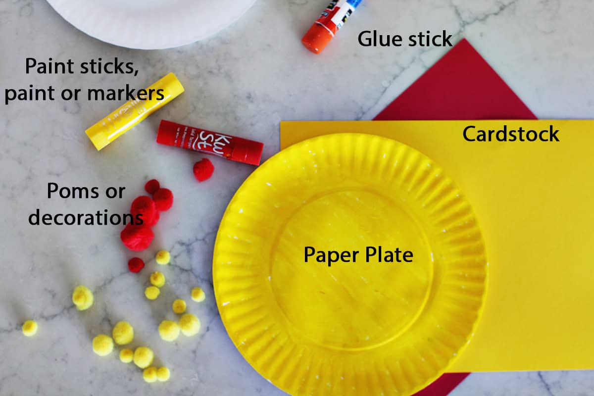 yellow paper plate, cardstock, paint and red paint sticks and a glue stick on a counter.