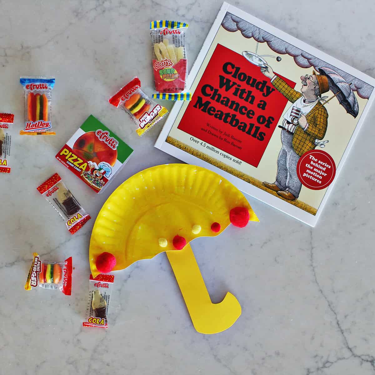 yellow paper plate made to look like an umbrella next to a book and gummy candies on a counter.
