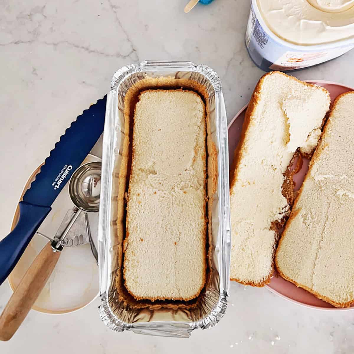 Pound cake container with one layer of cake added back to it next ot a knife and ice cream scoop.