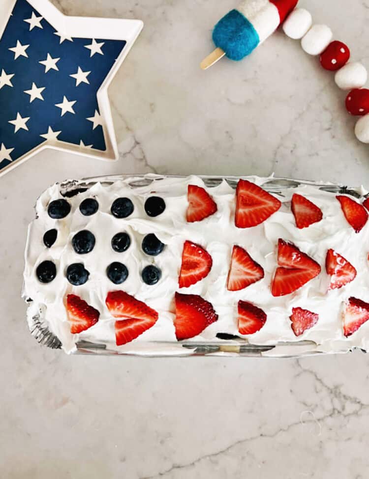 Overhead view of a pound cake topped with coolwhip, strawberries and blueberries to look like an American flag.