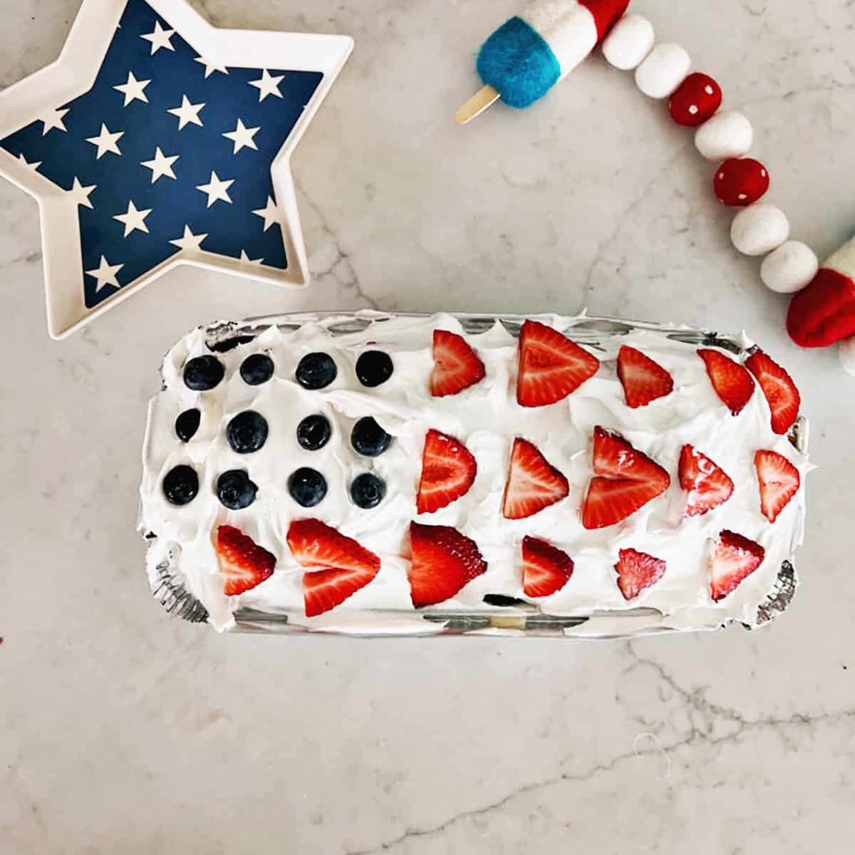 Overhead view of a pound cake topped with coolwhip, strawberries and blueberries to look like an American flag.
