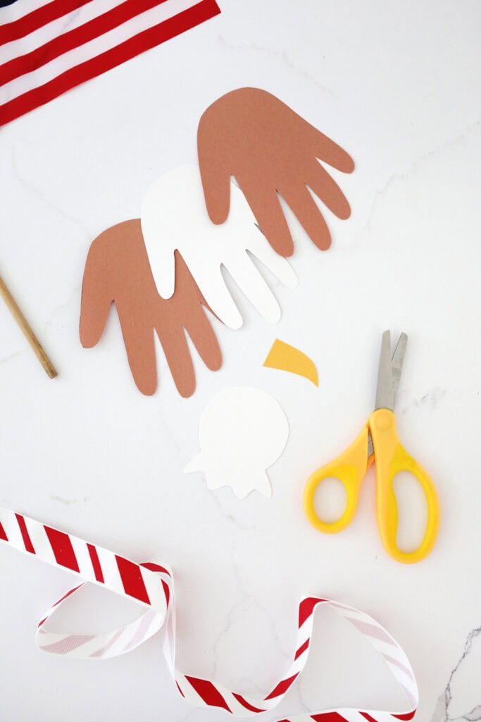 handprints cut from brown and white cardstock on a counter next to a cut out beak and eagle head shape on a counter to make an eagle handprint craft.