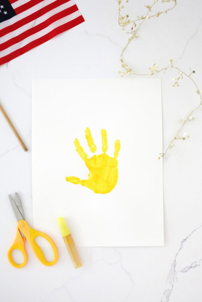 Yellow handprint on a white piece of cardstock on a counter.