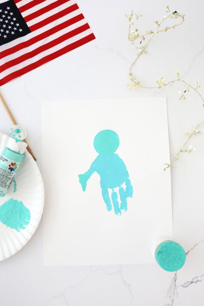 Turquoise handprint on a white piece of paper on a counter with a circle painted near the palm of the hand.