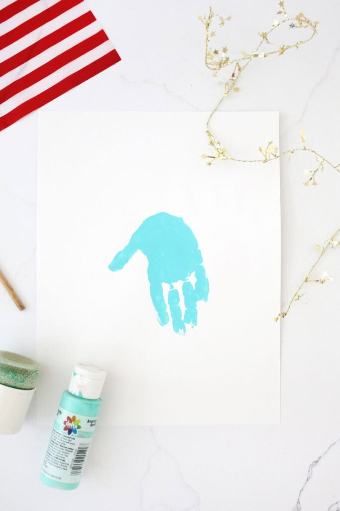 Turquoise handprint on a white piece of paper on a counter.