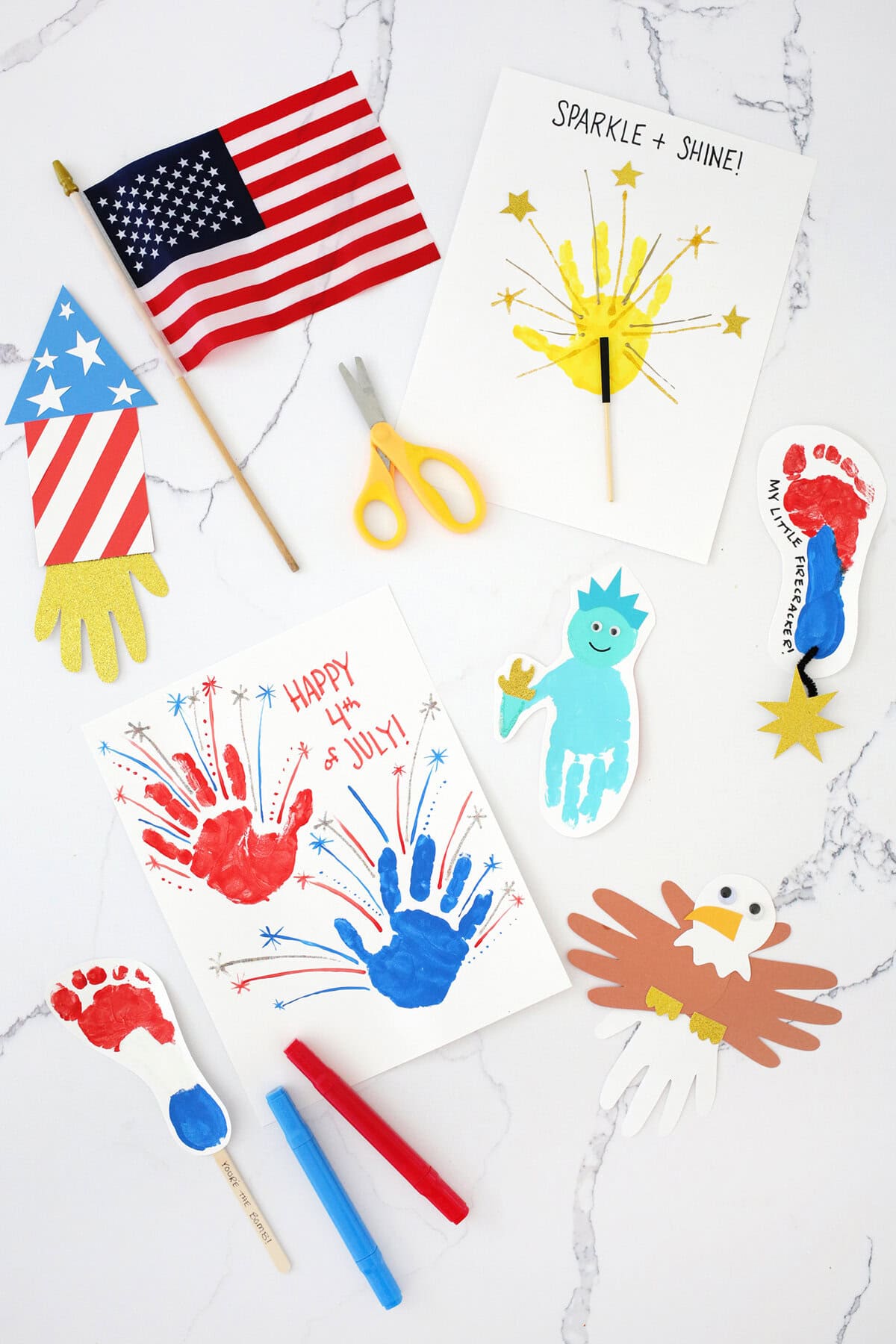 Fourth of July handprint crafts on a counter next to a pair of yellow scissors and a small American flag.