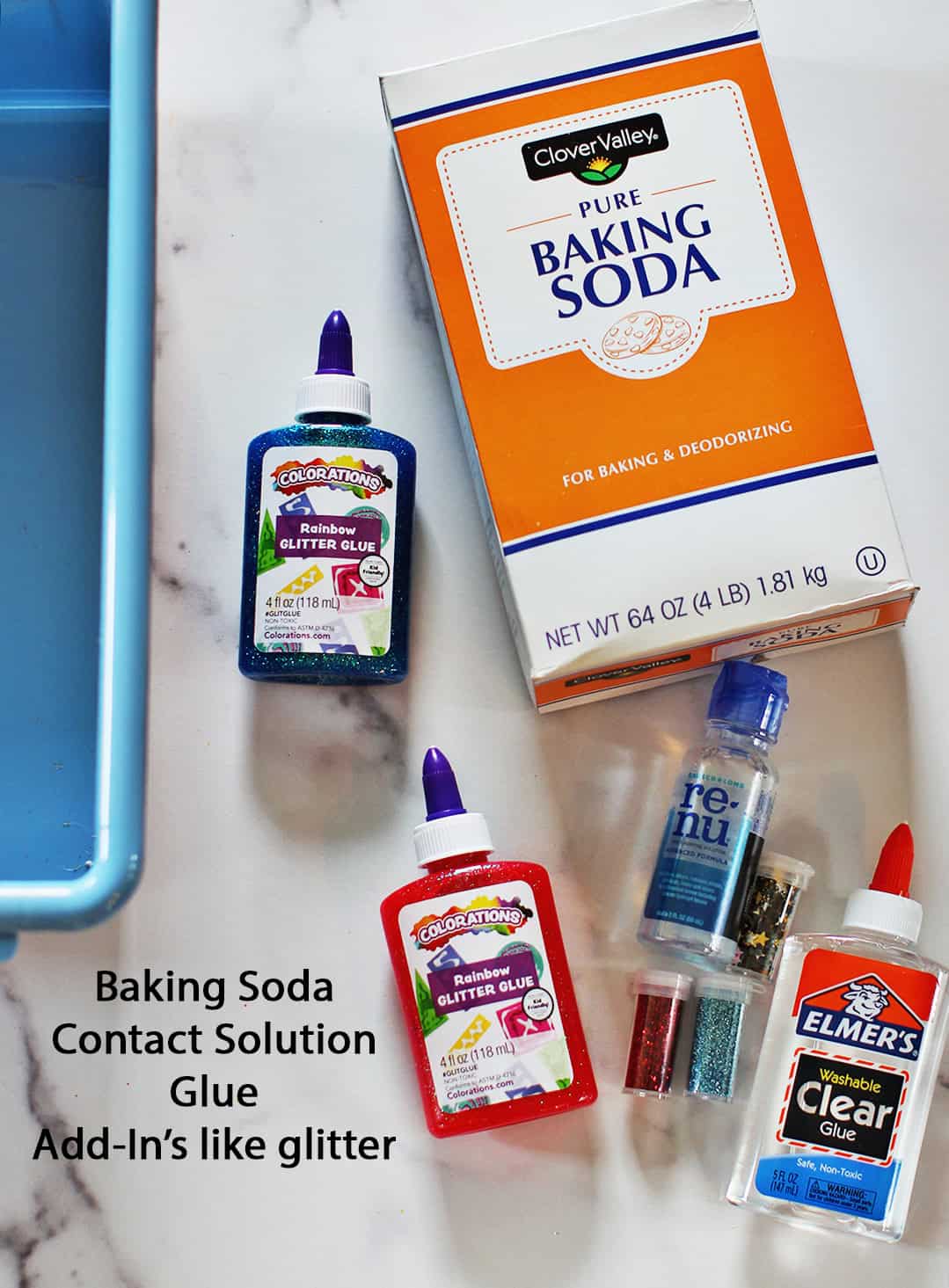 A box of baking soda, blue and red glitter glue, contact solution, clear glue and a blue container sitting on a counter.