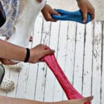 kids hands pulling apart blue glitter slime, red glitter slime and white fluffy slime.