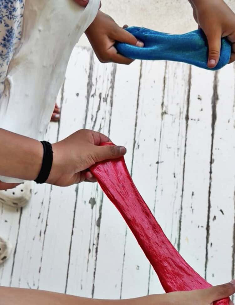 kids hands pulling apart blue glitter slime, red glitter slime and white fluffy slime.