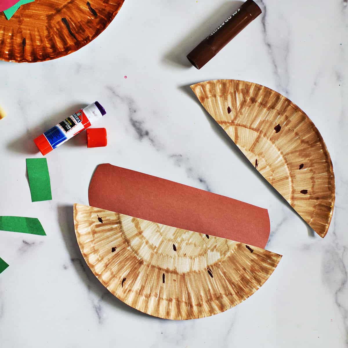 Brown construction paper piece being glued between two halves of a paper plate to look like a hamburger.