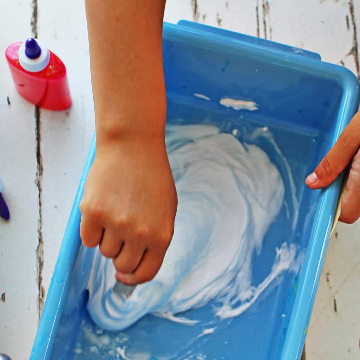 Child's hand mixing together glue, shaving cream and contact solution to make slime.