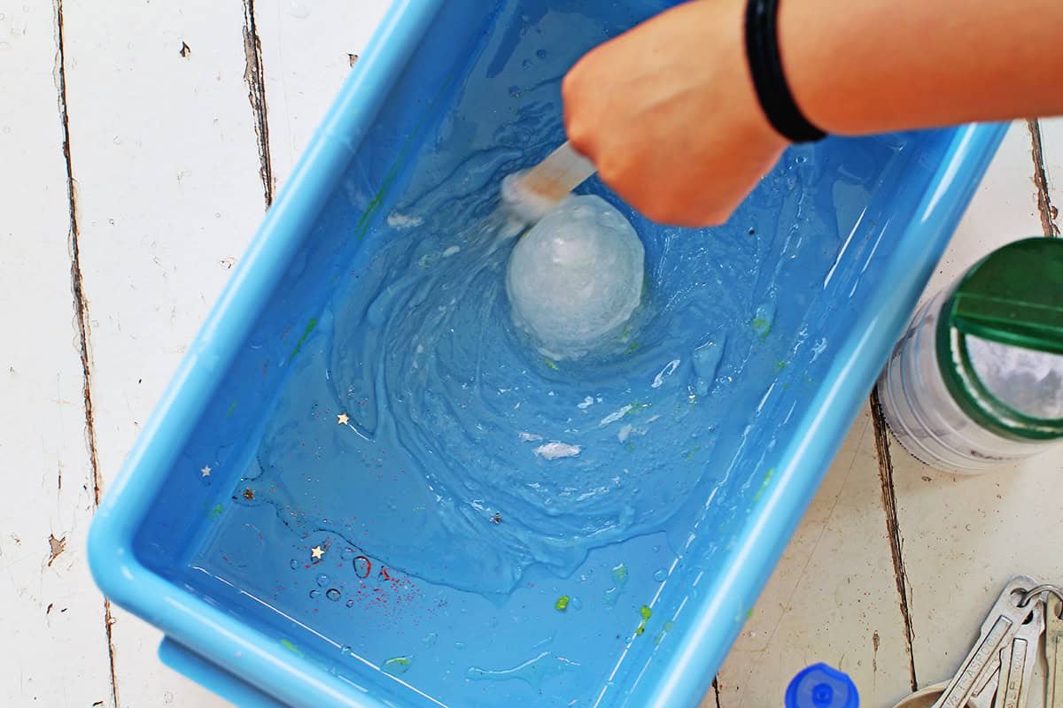 Child's hand stirring together clear glue, baking soda and contact solution to make slime.
