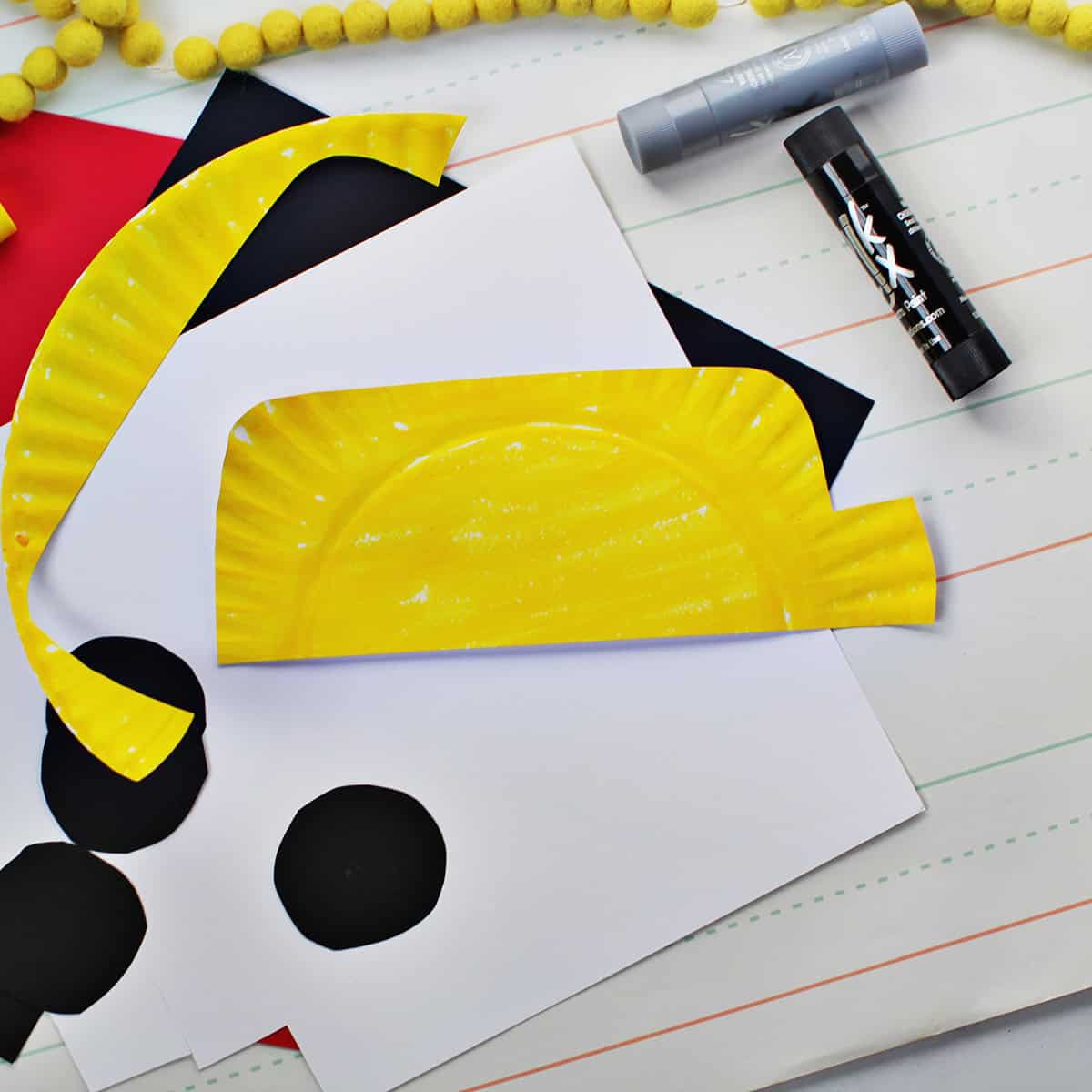 Paper plate painted yellow sitting on top of black cardstock circles and a piece of white cardstock.