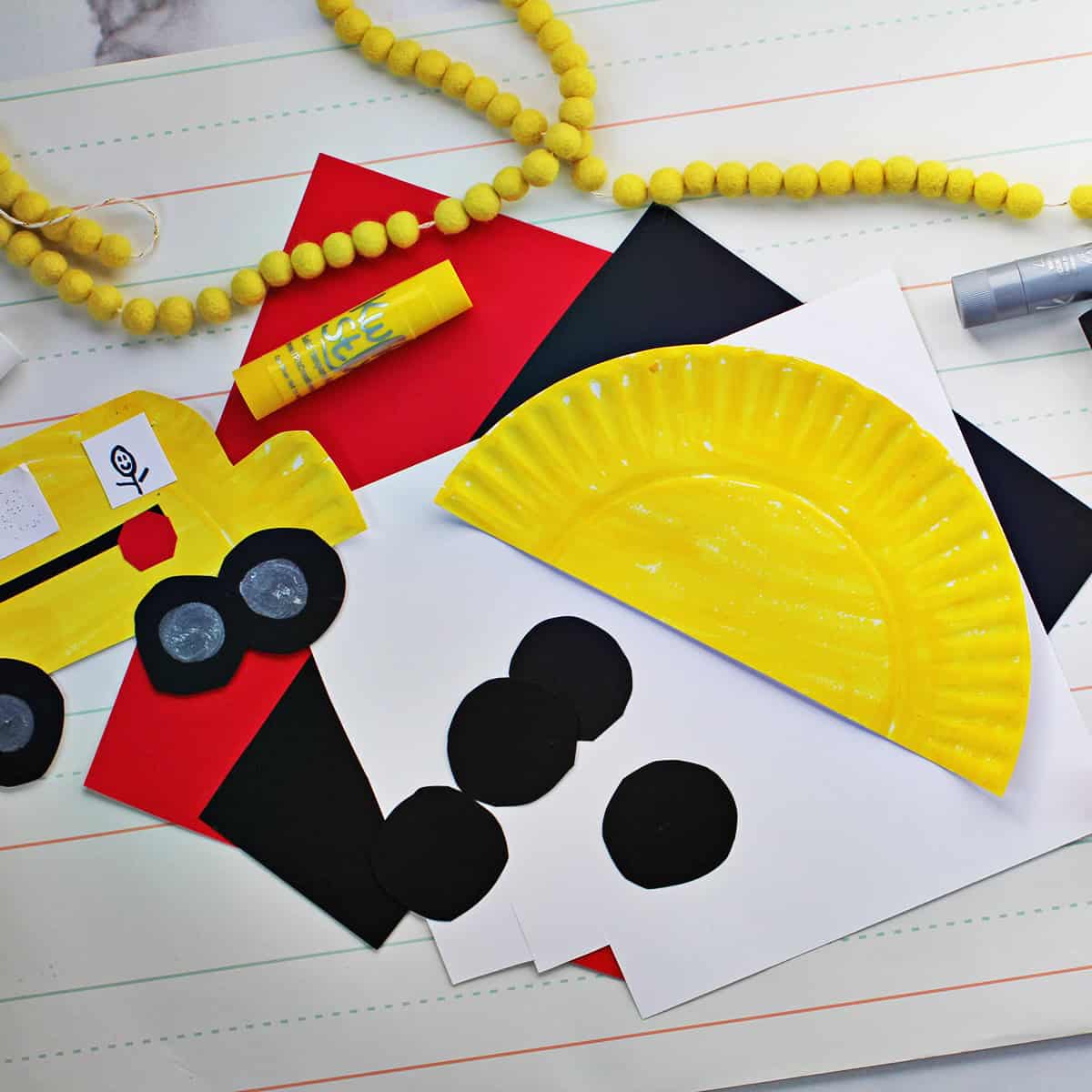 Paper plate cut in half and painted yellow next to black cardstock circles on top of red, white and black cardstock.