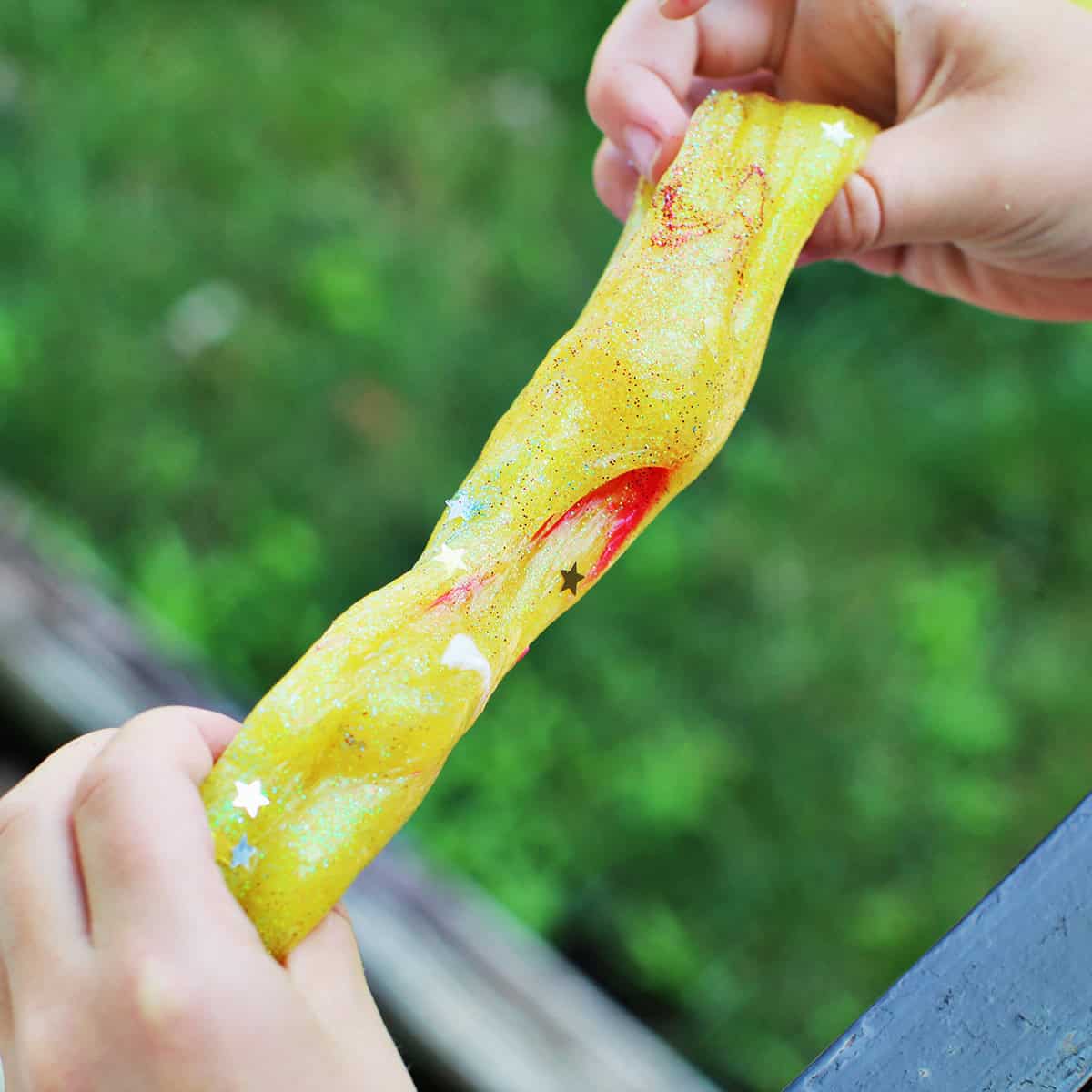 Child's hands pulling apart yellow slime.