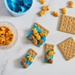 graham crackers with blue frosting, gold fish crackers, and nerd clusters next to a container of blue frosting.