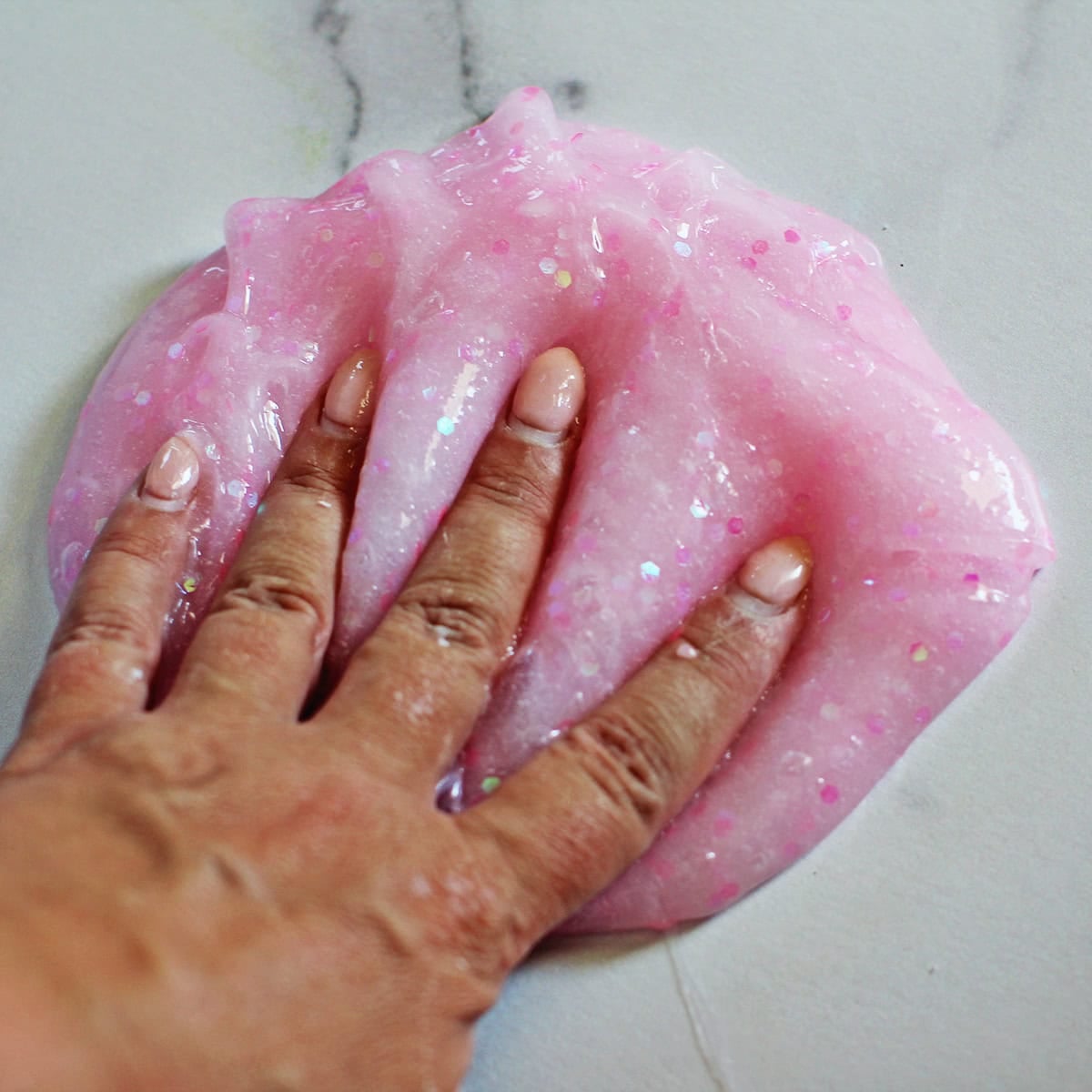 Hand pressing into pink glitter slime.