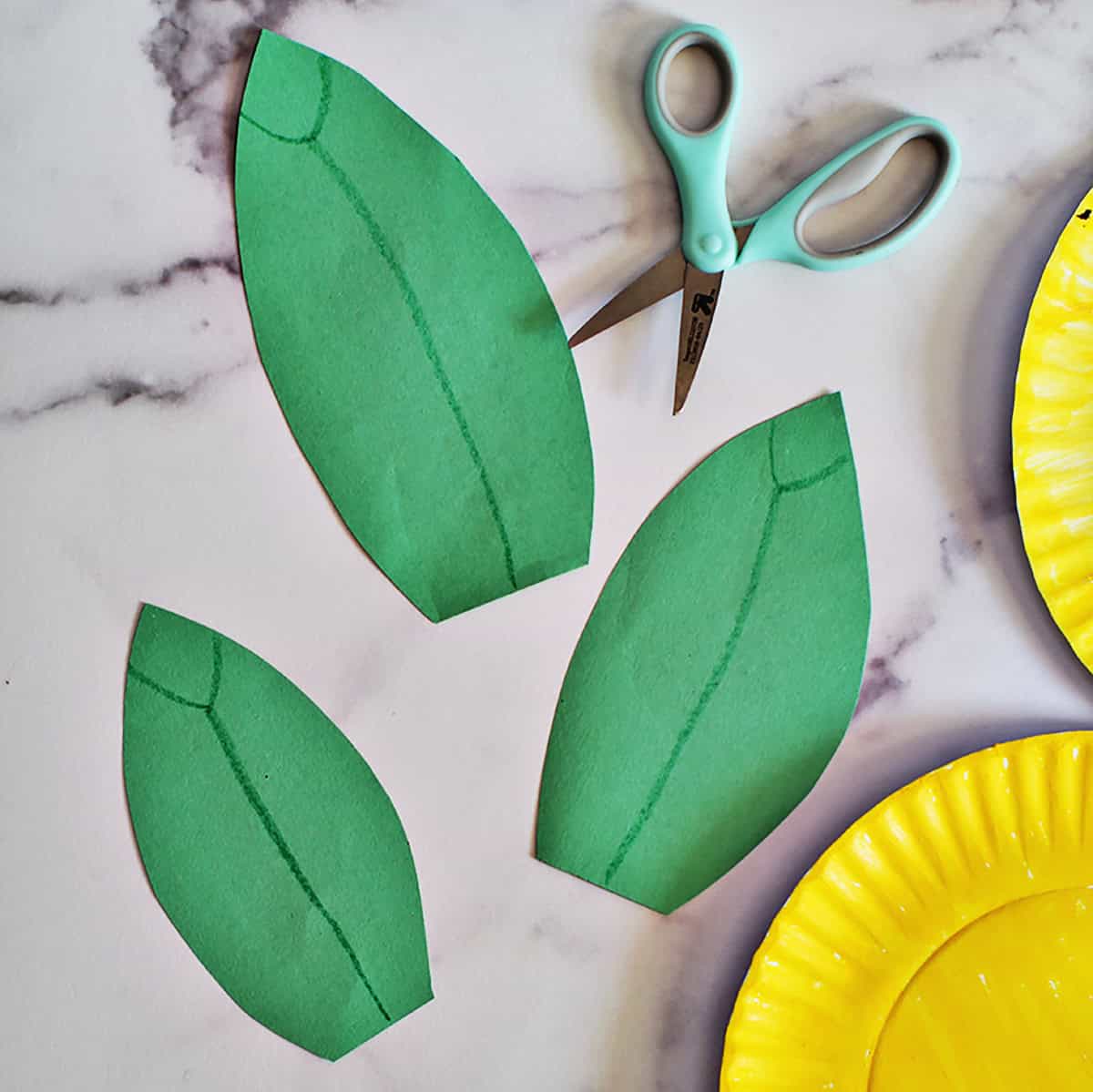 Green construction paper leaves next to kid's scissors on a counter.