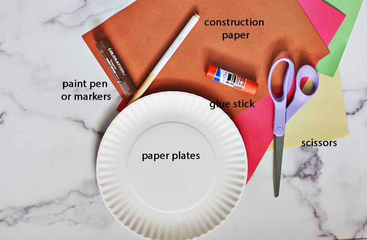 Paper plate, purple scissors, glue stick, marker and construction paper on a counter.