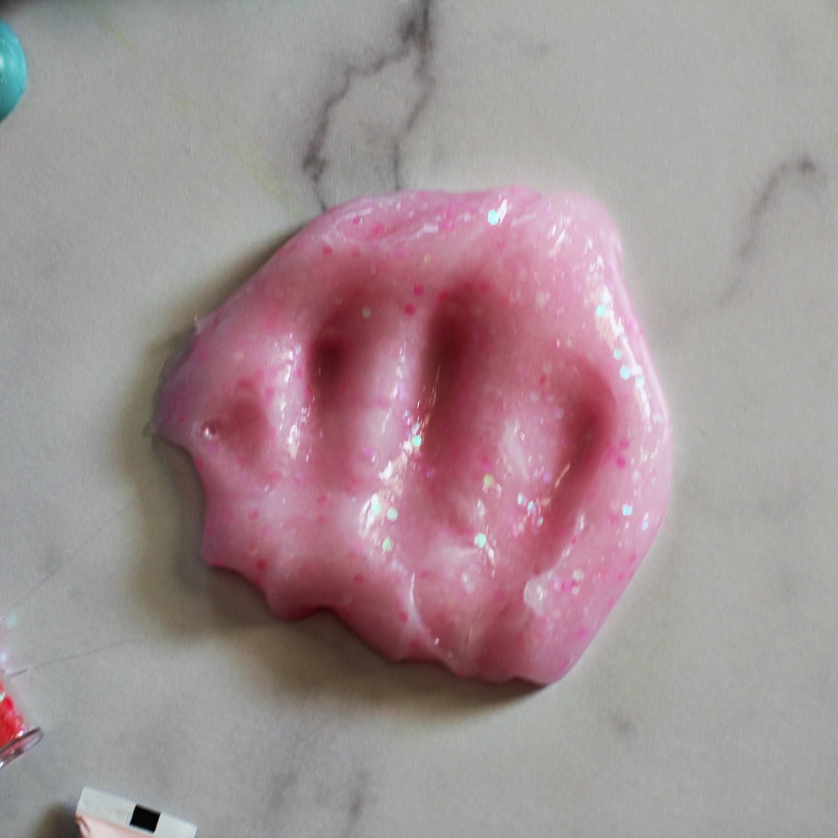 Pink glitter slime on a counter with fingerprints on it.