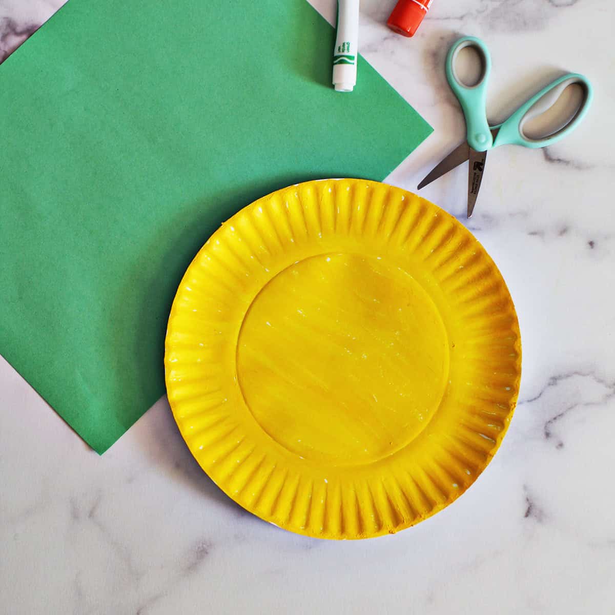 Yellow paper plate on a counter next to a piece of green construction paper.