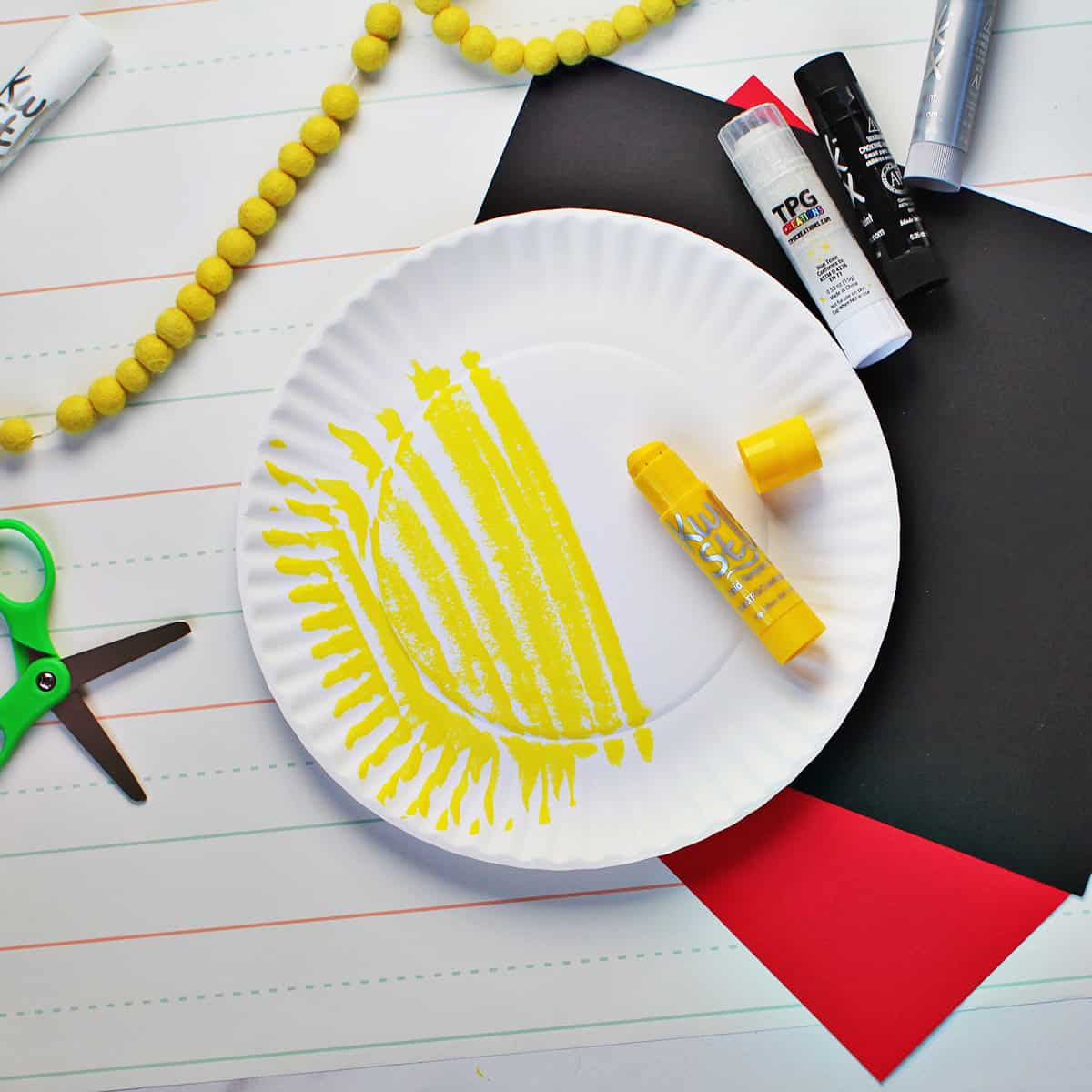 White paper plate being painted on with a yellow paint stick.