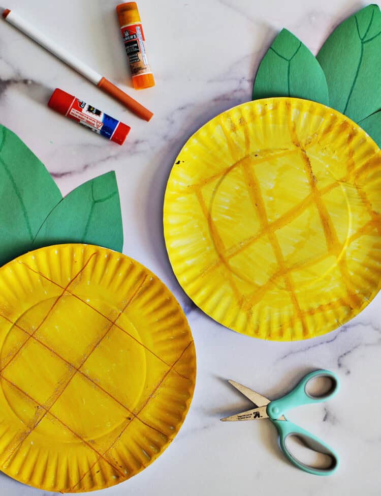 Two paper plates crafted to look like pineapples on a counter.