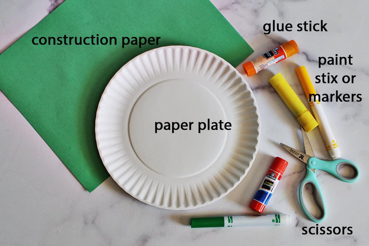 Green construction paper, glue stick, scissors, marker and a paper plate on a counter.