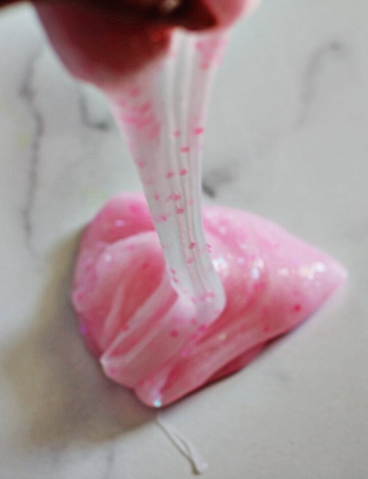 Hand pulling pink glitter slime off a counter.