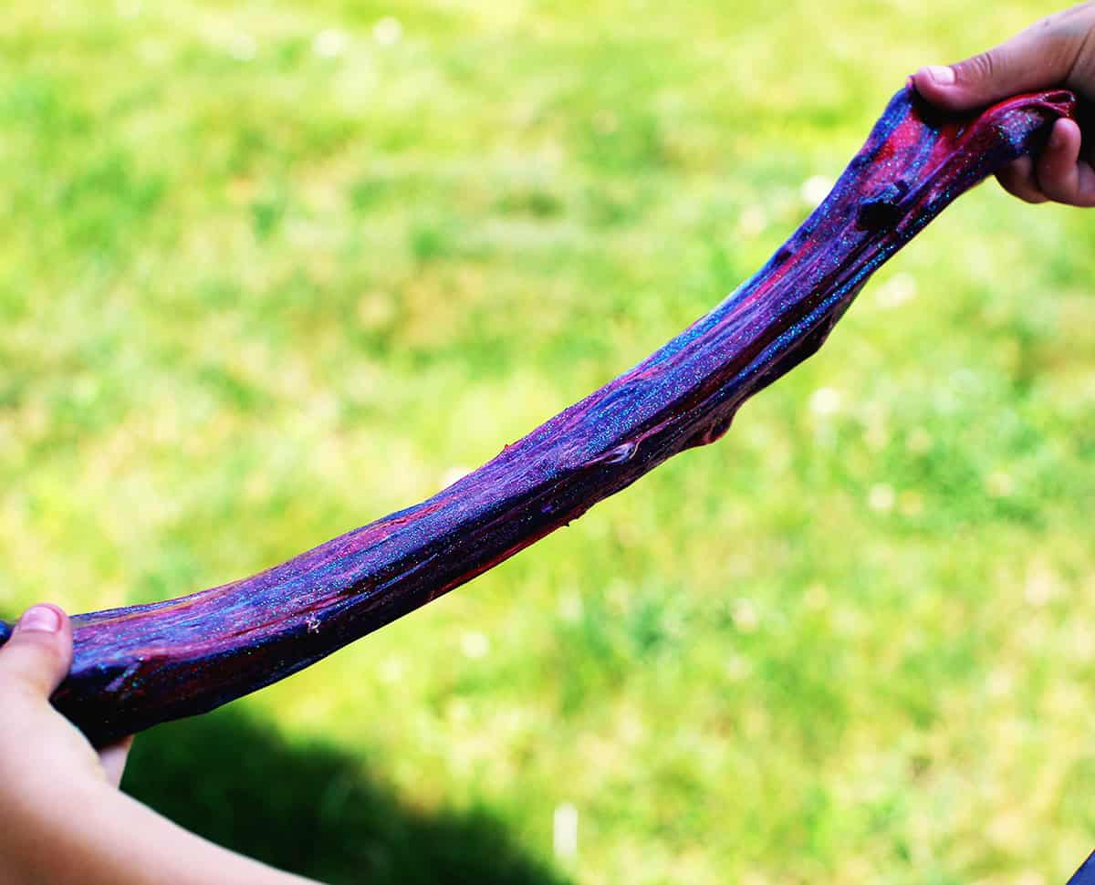 Hand stretching apart purple sparkly slime.