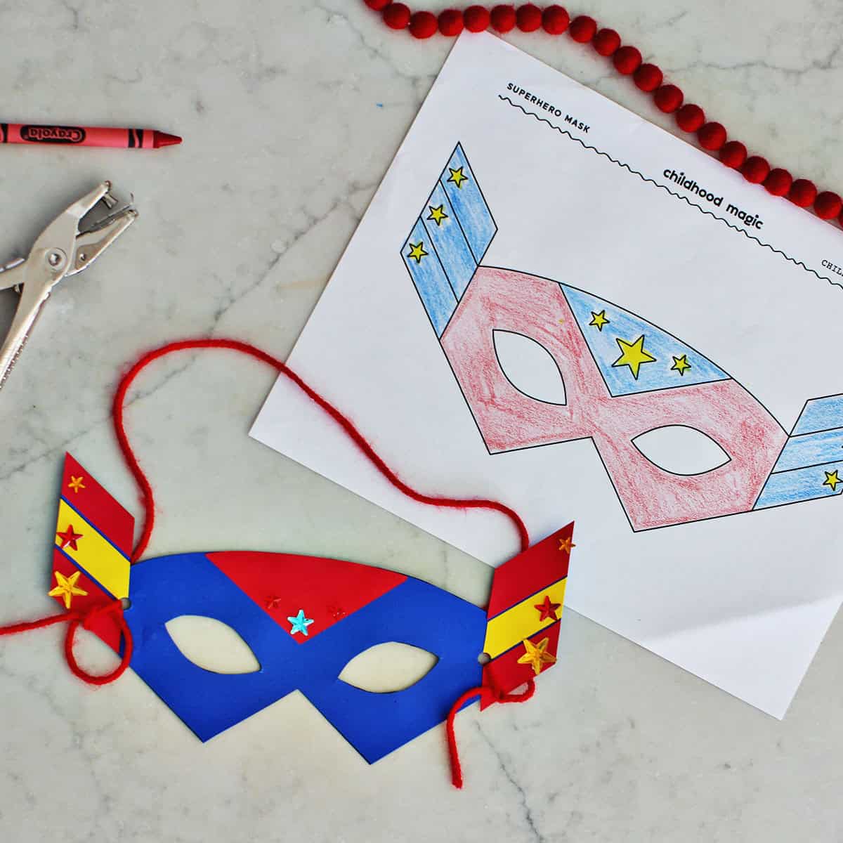 cut out paper mask with yarn string next to a coloring page of a superhero mask for kids.