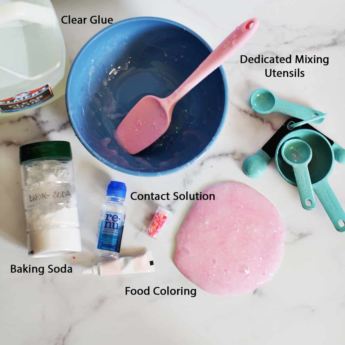 Clear school glue, blue plastic bowl, pink spatula, teal measuring utensils, baking soda, contact solution, food coloring and pink glitter slime on a counter.