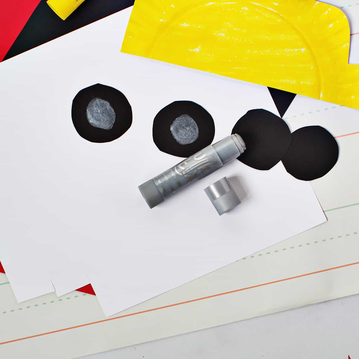 Silver metallic paint stick being used to draw circles on the black cardstock circles to make it look like a tire.