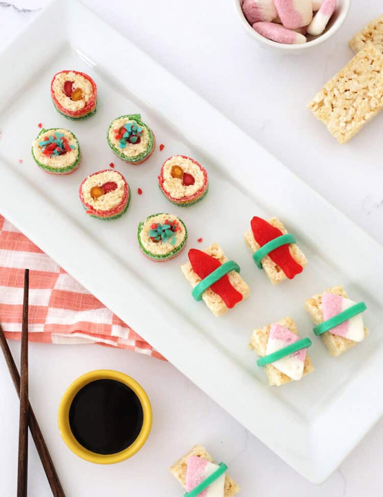 sushi candy madefrom rice krispie treats and other candies next to chop sticks and a small bowl of chocolate syrup.
