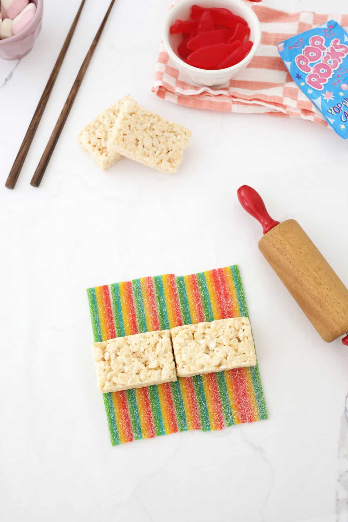 two rice krispie treats sitting on top of airhead extremes next to a rolling pin.