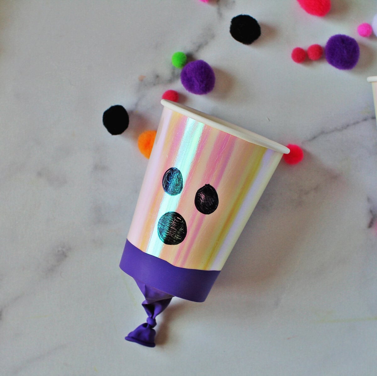 Cup with a balloon wrapped around the bottom to shoot out pom poms and decorated to look like a ghost.