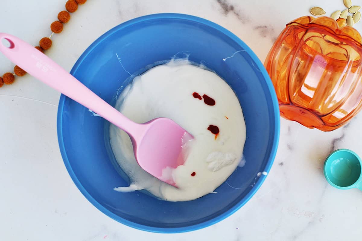 Orage gel food coloring being added to homemade slime in a blue bowl.