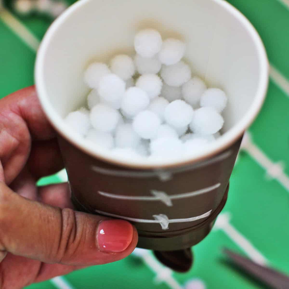 brown cup decorated to look like a football full of mini pom poms.