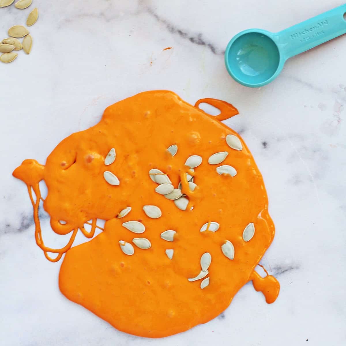 orange slime on a counter with pumpkin seeds being added to it.