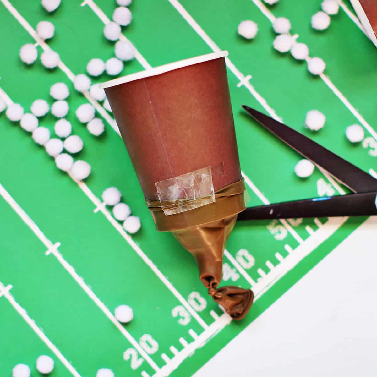 tape holding a cut balloon onto a brown paper cup.