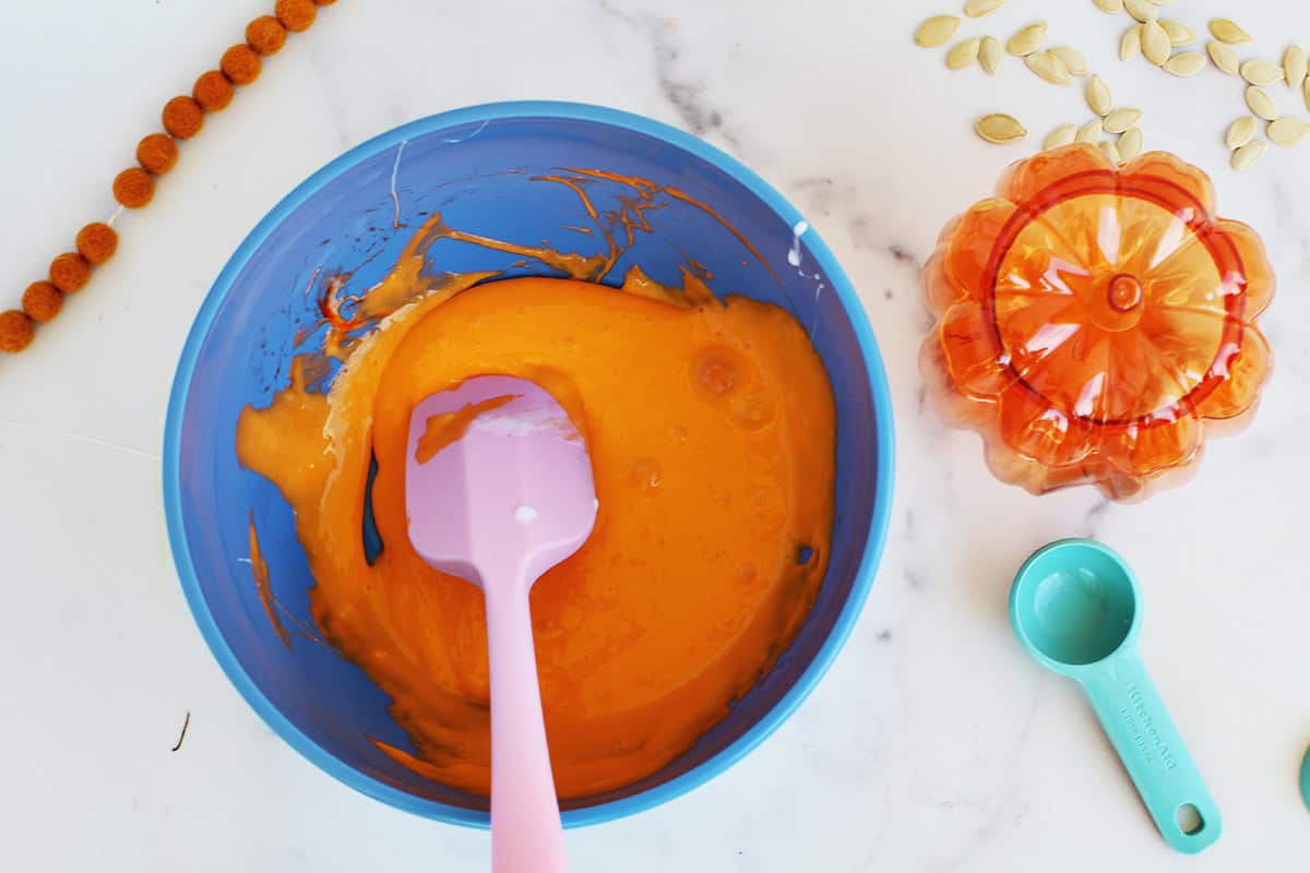 Orange slime being stirred in a blue bowl with a pink spatula.