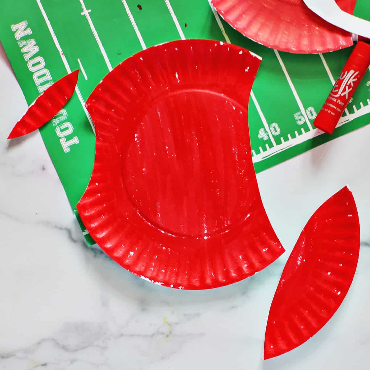 Red paper plate being cut to make the shape of a football helmet.