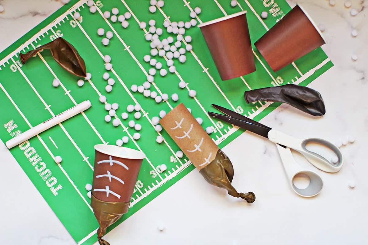 pom pom shooters made with brown cups and brown balloons to look like footballs on a football field placemat.